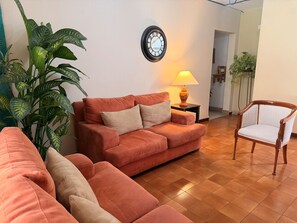 Una sala de estar con sofá, una silla, una lámpara y un reloj en la pared.