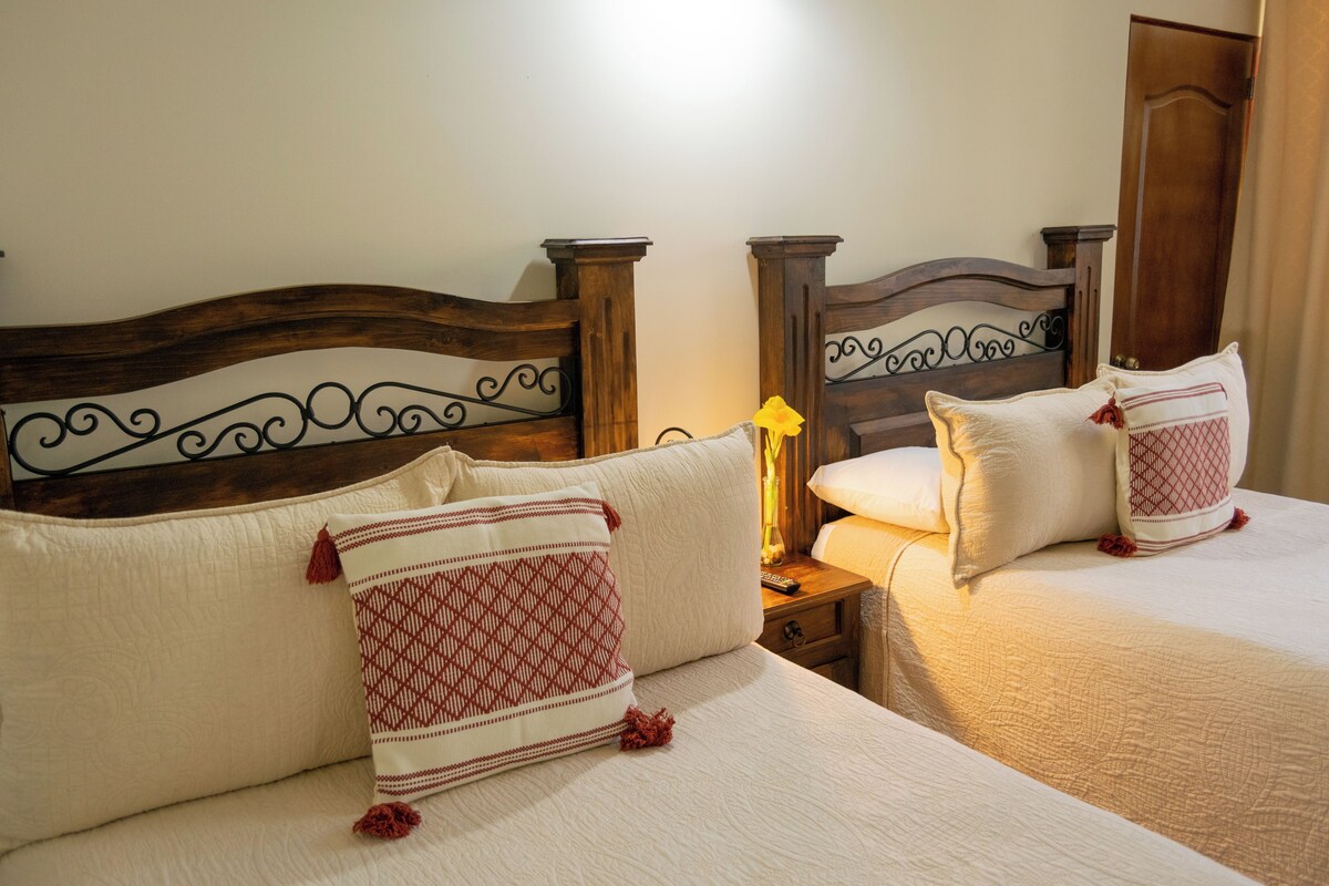 A hotel room with two beds, wooden headboards, and a nightstand with a lamp.