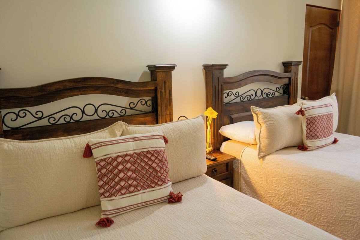 A hotel room with two beds, wooden headboards, and a nightstand with a lamp.