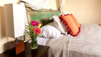 A bed with a white and orange pillow, a vase with flowers, and a bedside table with a lamp.