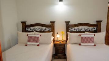 Uma cama de casal com cabeceira de madeira, mesa de cabeceira com abajur e um vaso com flor.
