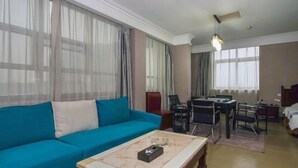 Una sala de estar con un sofá azul, una mesa de centro, una mesa de comedor con sillas y una cama al fondo.
