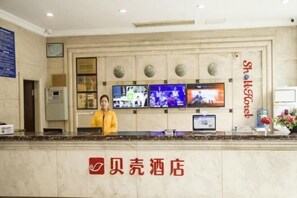 Ein Hotel-Empfangsbereich mit Rezeptionist, mehreren Fernsehern und einem Schild mit dem Hotelnamen.
