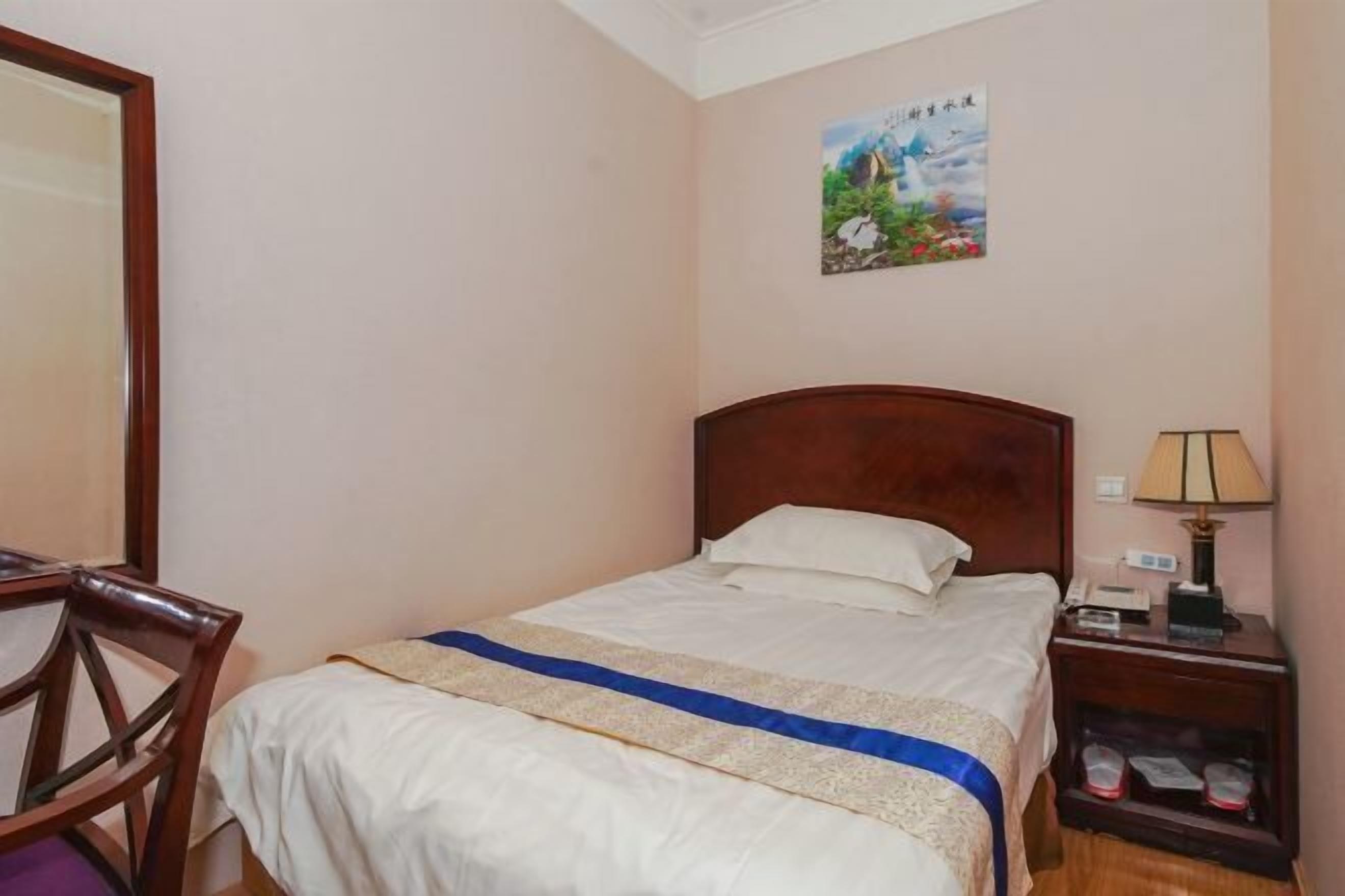 A neatly made bed with a wooden headboard, a bedside table with a lamp, and a chair.