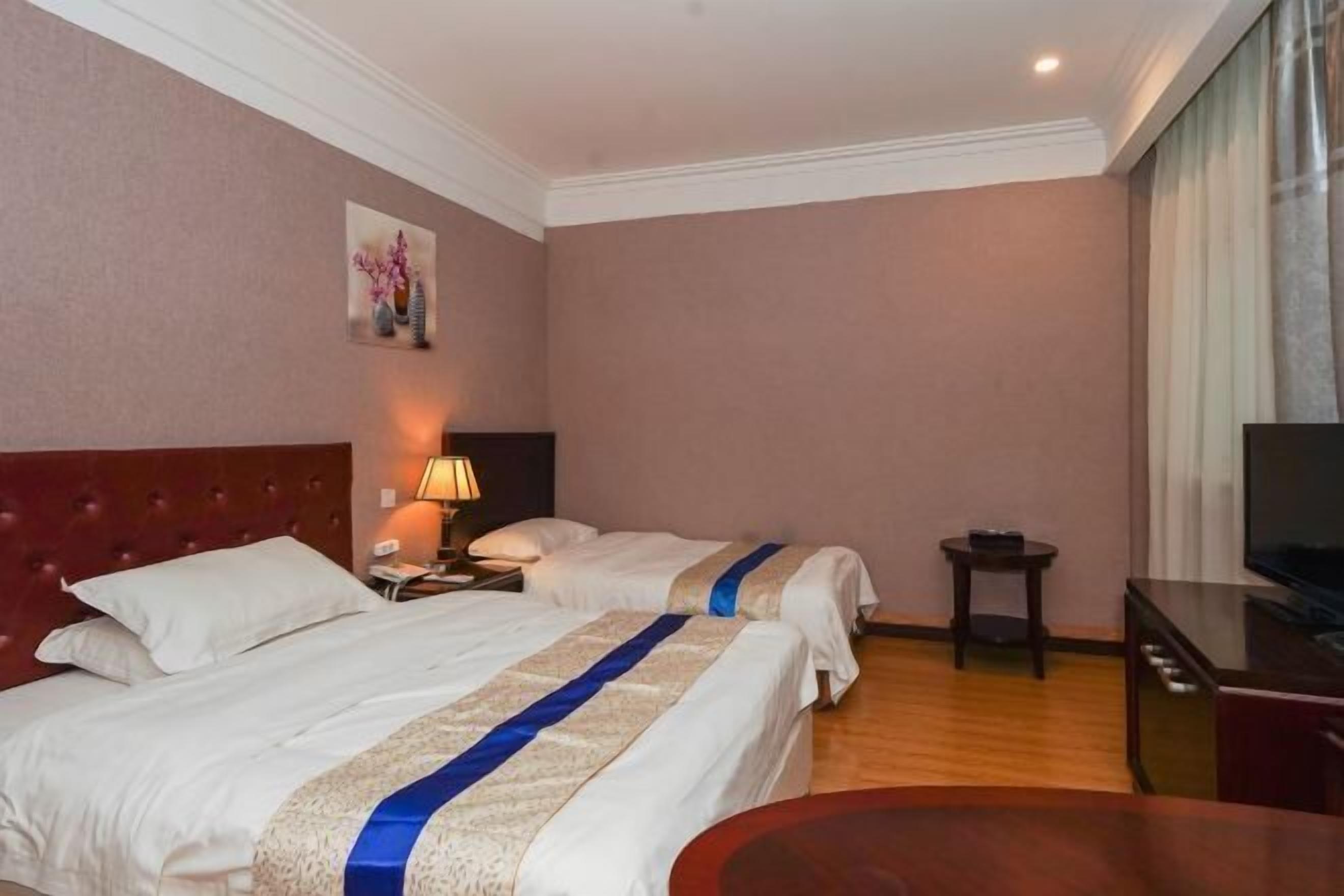 Quarto de hotel com duas camas, televisão, escrivaninha e uma mesa pequena.