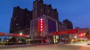 Un hotel de varios pisos, con un llamativo letrero rojo y una calle concurrida con semáforos.