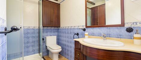 Ein Badezimmer mit Duschkabine, Toilette, Waschbecken mit Unterschrank und Spiegel.