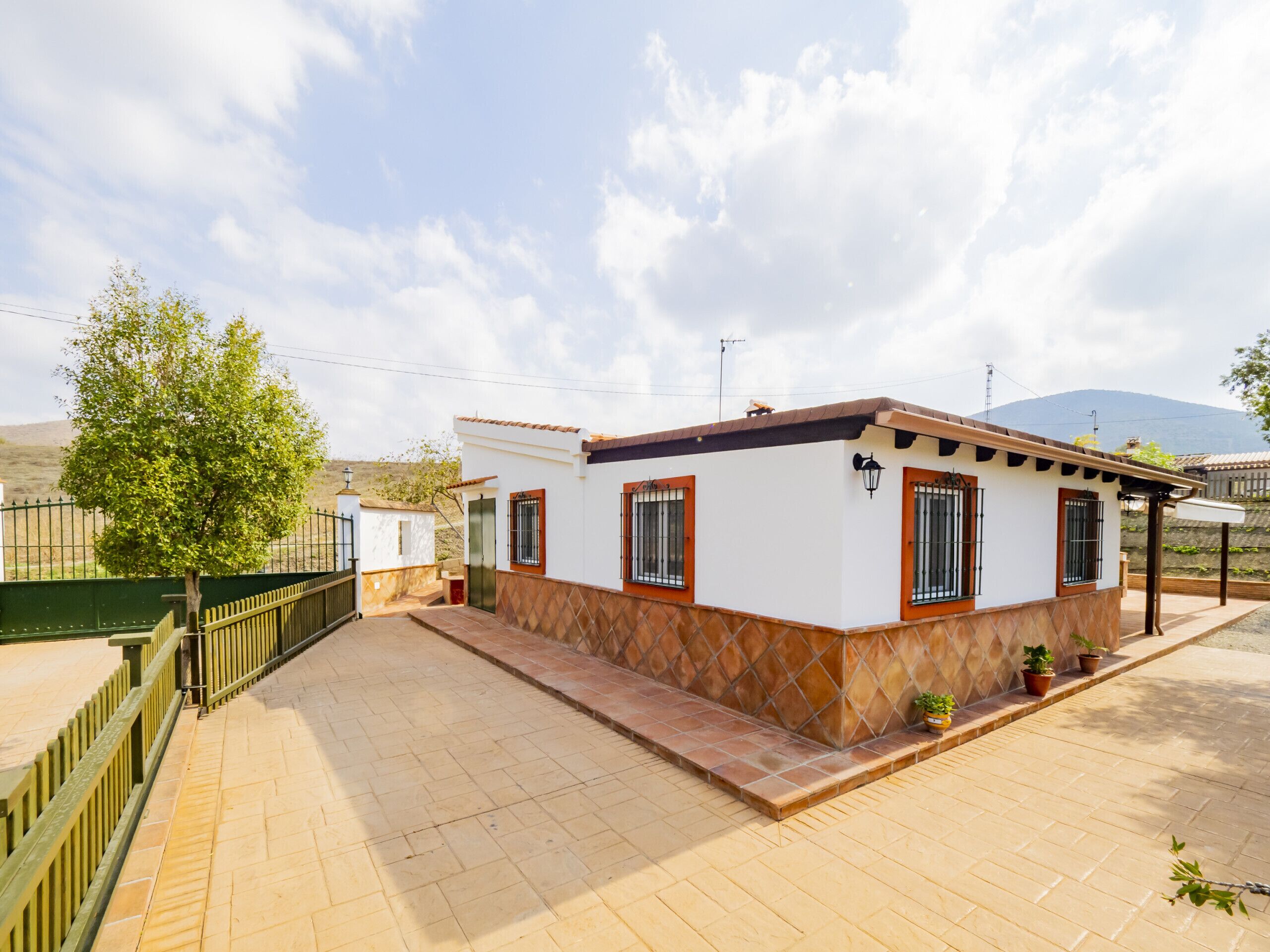 A two-story house with a tiled patio, a green fence, and a mountain in the background.