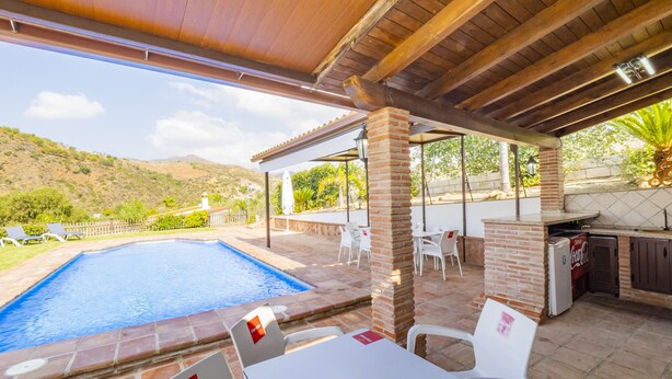 Un área de piscina exterior con un patio cubierto, asientos y un refrigerador de Coca-Cola.