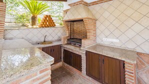 Cocina exterior con horno de ladrillo, encimeras de granito y armarios de madera.