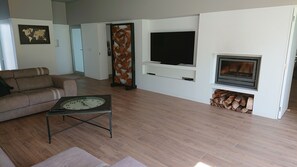 A modern living room with a sofa, a coffee table with a clock, a flat-screen TV, and a fireplace. - Lux Private Villa  (Rabo de Peixe)