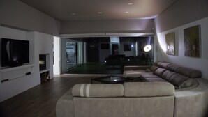 Ein modernes Wohnzimmer mit einem großen Ecksofa, einem Flachbildfernseher und einer Glastür, die in einen Essbereich führt.