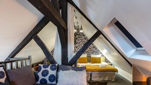 Ein gemütliches Schlafzimmer im Dachgeschoss mit freiliegenden Holzbalken, einem Bett mit gelber Decke und einer Treppe, die zum oberen Stockwerk führt.