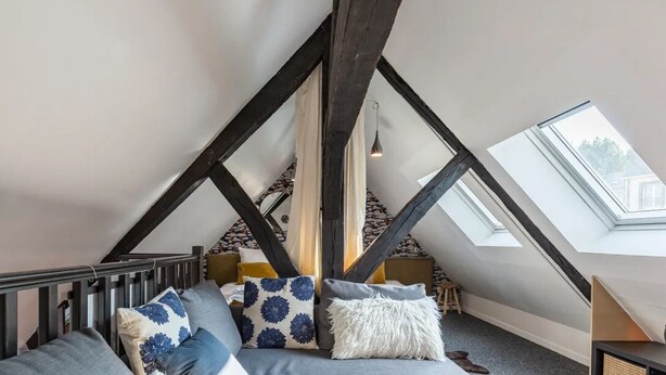 Ein gemütliches Schlafzimmer im Dachgeschoss mit schrägen Wänden, einem Bett mit gemusterten Kissen und Dachfenstern.