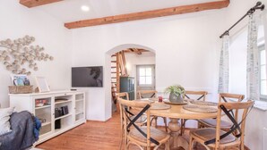 A dining area with a wooden table and chairs, a white cabinet with a television, and a decorative wall piece. - House Bella (Bohinjska Bela)