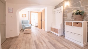 A hallway with wooden flooring, a light blue armchair, a white bench, and a stone wall. - House Bella (Bohinjska Bela)