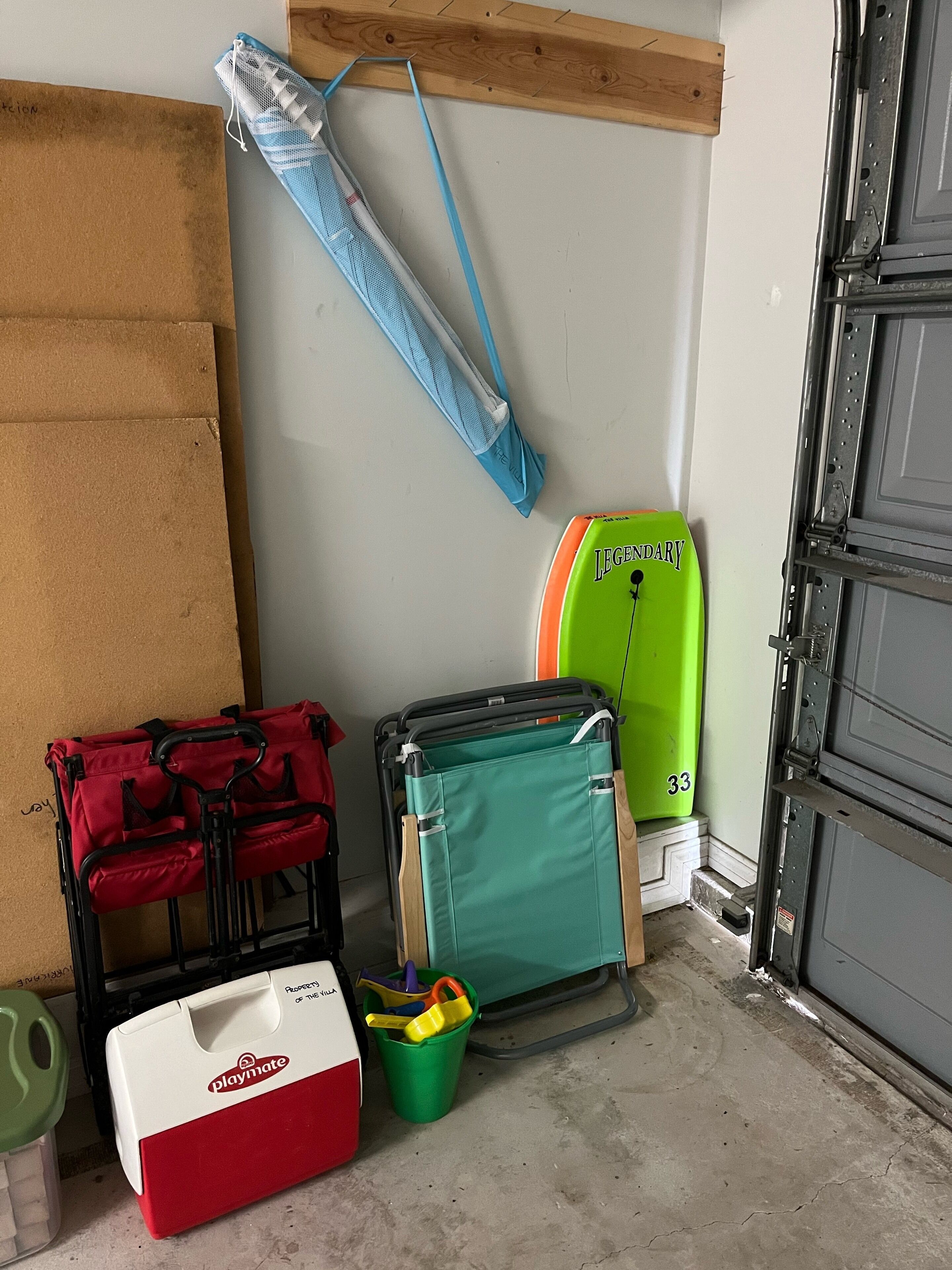 A storage area with a red cooler, a green storage bin, a blue mesh bag, and a green suitcase.