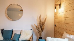 Una habitación acogedora con un espejo redondo, una pared de madera, un sofá con cojines azules y blancos y un jarrón con plantas secas.