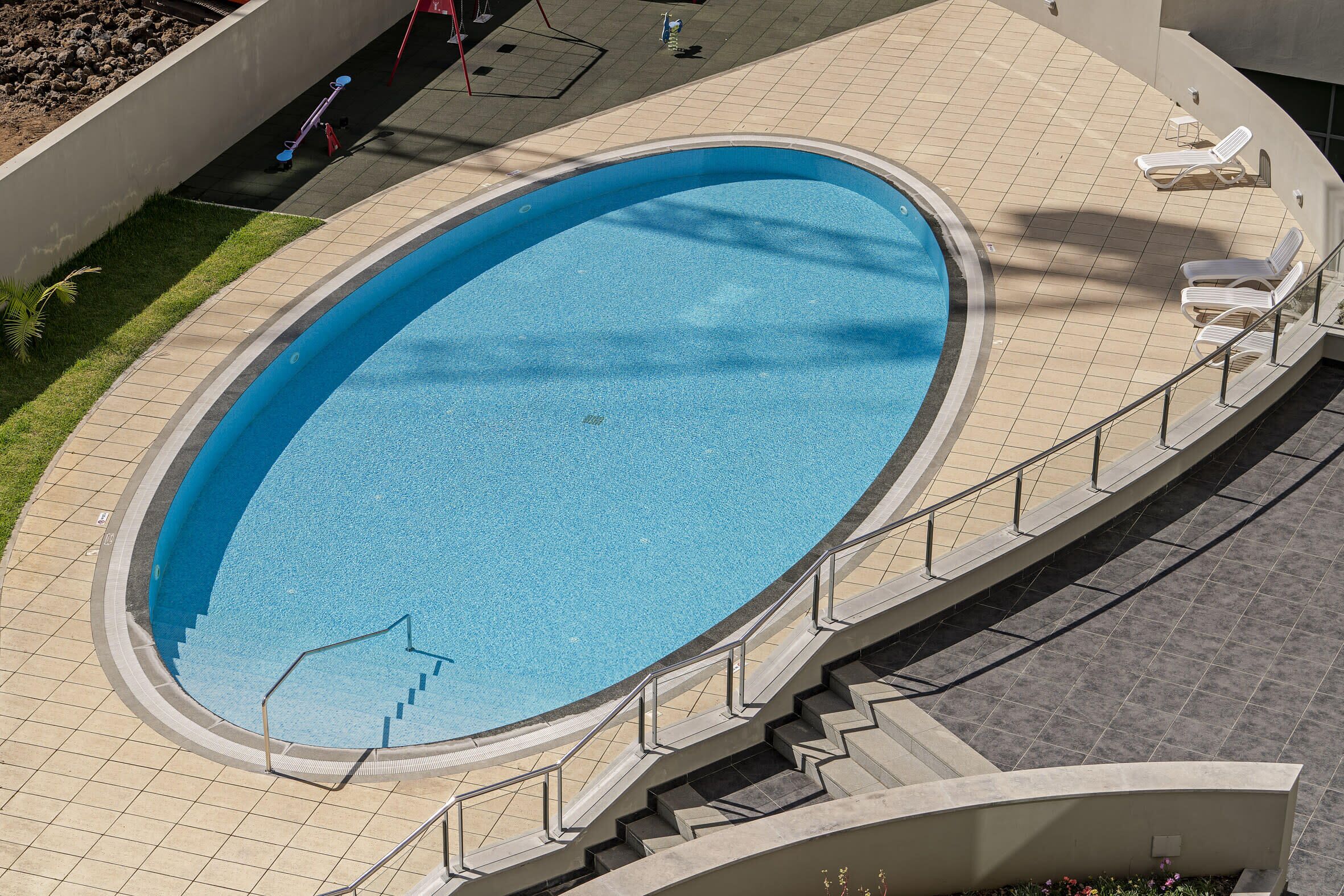 Una piscina exterior de diseño curvo, rodeada por una solana con baldosas y una escalera que baja a la piscina.