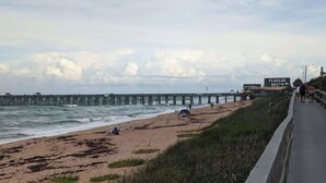 Una playa con un muelle que se adentra en el océano, un letrero que dice "FLAGLER BEACH" y un paseo marítimo a lo largo de la orilla.