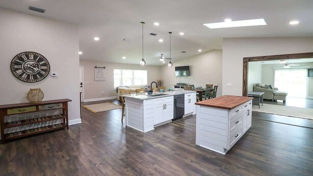 Una cocina amplia con una isla central, armarios blancos y un reloj de pared grande.