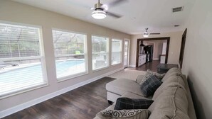 Un salón amplio con sofá color beige, ventanas grandes y ventilador de techo.