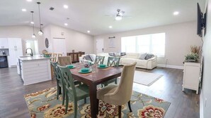 Amplia sala de estar con mesa de comedor, sillas y sofá. Incluye una zona de cocina con armarios y encimera.