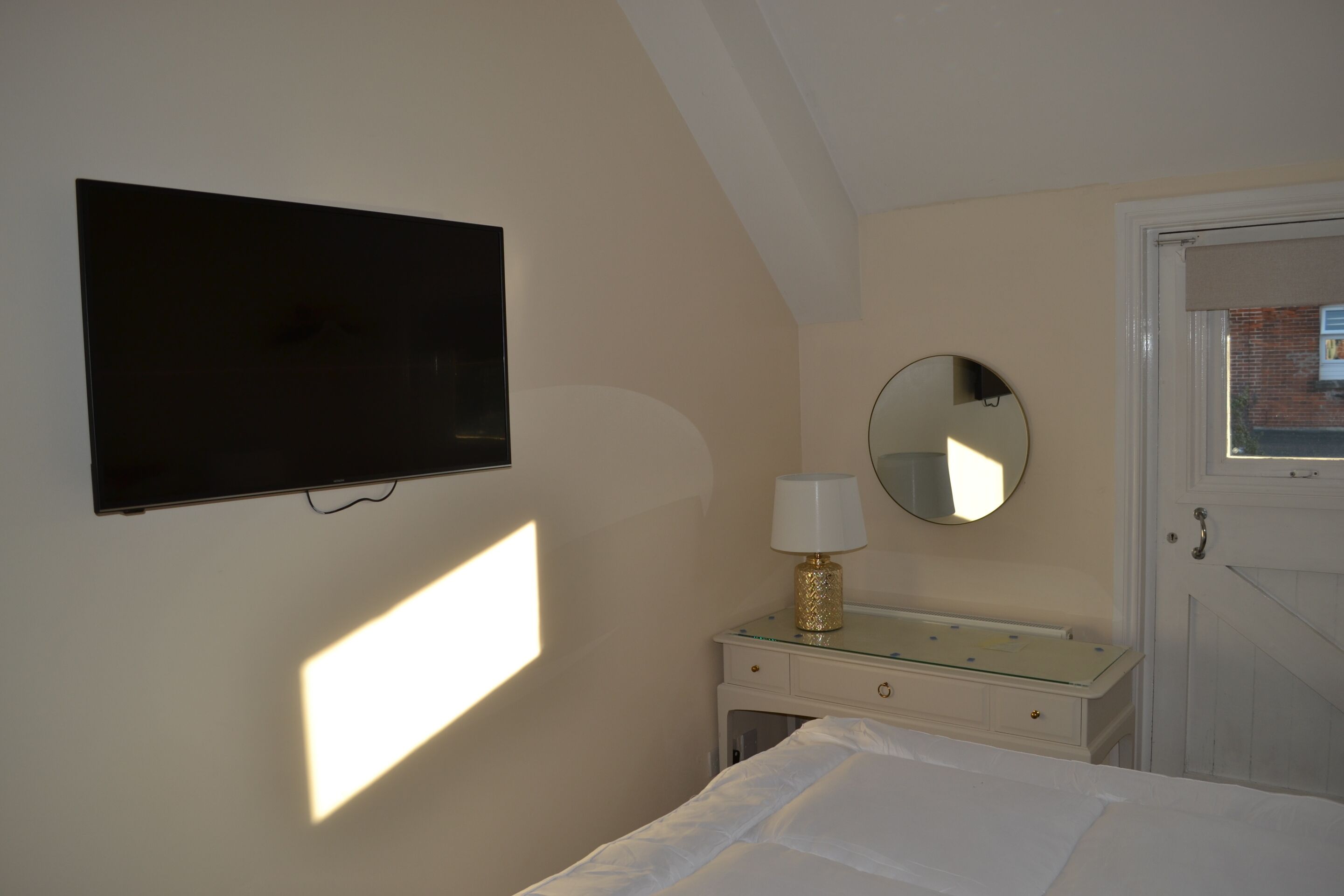 Une chambre à coucher avec un lit, une table de chevet avec une lampe, un miroir et un téléviseur fixé au mur.