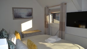 Een netjes opgemaakt bed met een raam, een flatscreen televisie en een schilderij aan de muur.