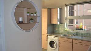 Een moderne keuken met een ingebouwde wasmachine, een raam met uitzicht en een ronde spiegel aan de muur.