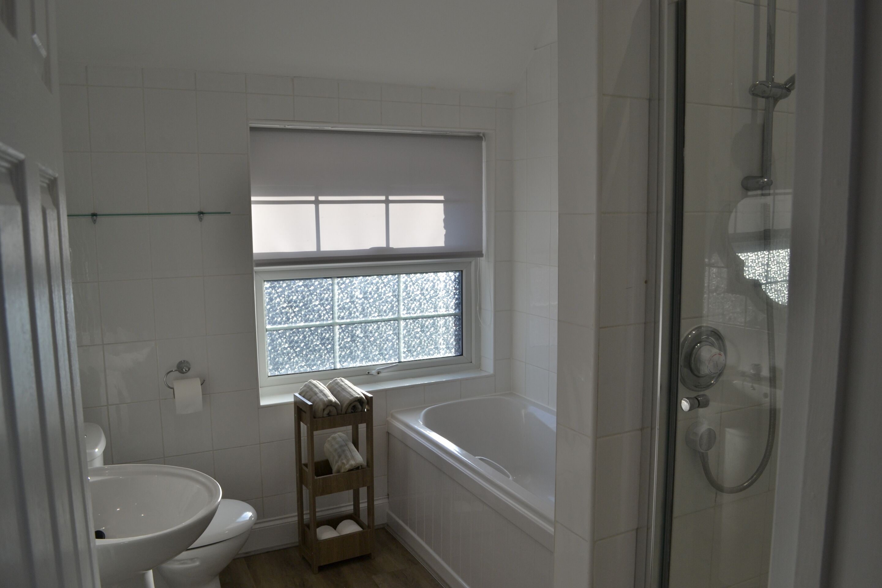 A bathroom with a toilet, sink, window, and shower.