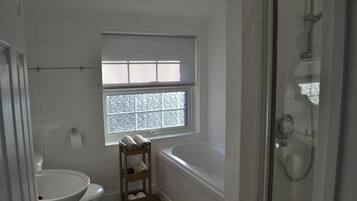 A bathroom with a toilet, sink, window, and shower.