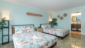 Una camera da letto con due letti, un comodino, una decorazione a forma di tavola da surf, uno specchio e un bagno visibile tramite una porta aperta.