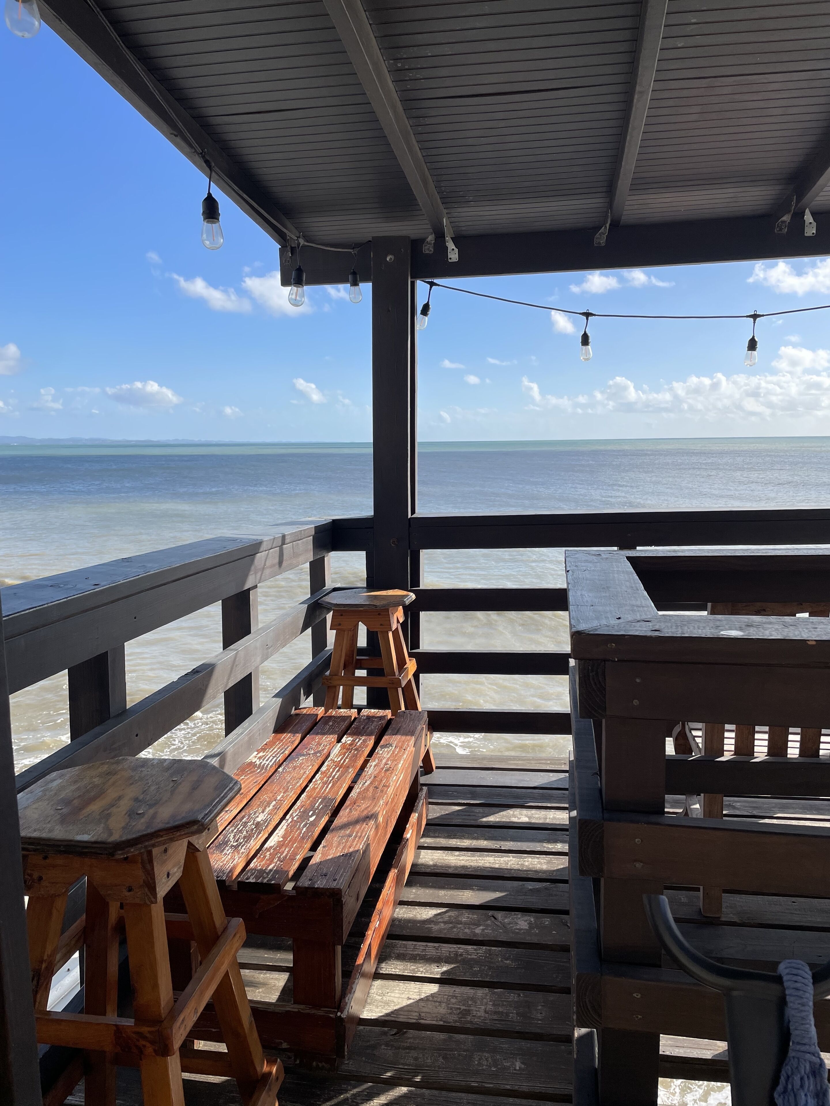 A wooden deck with benches and a table, overlooking a calm sea.