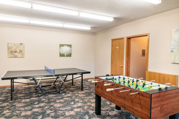 A room with a ping pong table, a foosball table, and two doors.