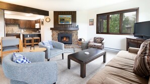 A living room with a fireplace, a television, and a kitchen in the background. - Remodeled Nice Top-Floor Condo. Hot Tub. Fireplace (Breckenridge)