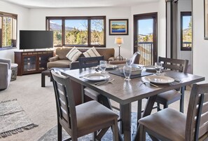 A dining area with a table set for four, a sofa, a television, and a window with a mountain view.