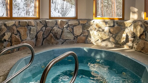 An indoor swimming pool with stone walls and windows overlooking a snowy forest. - Remodeled Nice Top-Floor Condo. Hot Tub. Fireplace (Breckenridge)