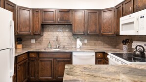 A kitchen with dark wooden cabinets, a marble countertop, a stainless steel range hood, and a white dishwasher. - Remodeled Nice Top-Floor Condo. Hot Tub. Fireplace (Breckenridge)