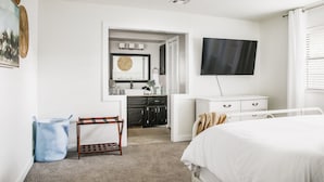 A bedroom with a bed, a TV, a bathroom with a sink and mirror, and a laundry area. - Cozy 3 bdrm w/pool & hot tub!! (Oklahoma City)