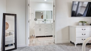 A bathroom with a white vanity, a mirror, and a television mounted on the wall. - Cozy 3 bdrm w/pool & hot tub!! (Oklahoma City)