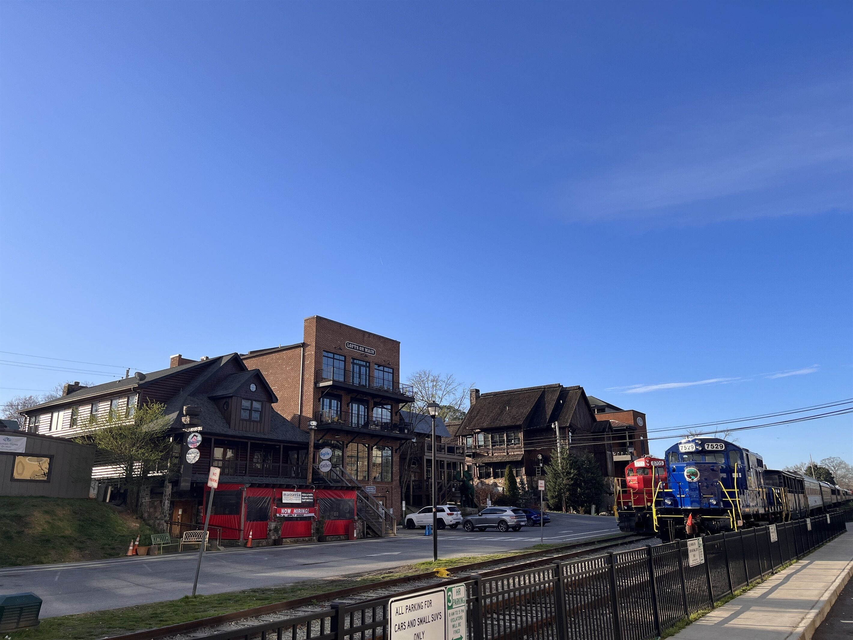 Une gare avec une locomotive bleue, un autobus rouge et un bâtiment sur lequel on peut lire l’inscription « LOFTS ON MAID ».