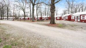 Un terrain de camping avec des cabanes rouges, des tables de pique-nique et des arbres.