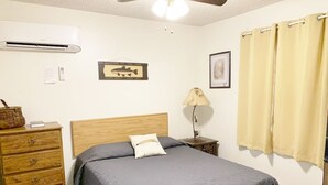 Une chambre à coucher comprenant un lit, une commode en bois, une table de chevet, une lampe et un ventilateur de plafond.