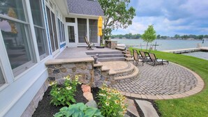 Une terrasse avec des marches en pierre menant à un espace de détente situé au bord d’un lac, entouré de verdure et délimité par un mur de pierre.