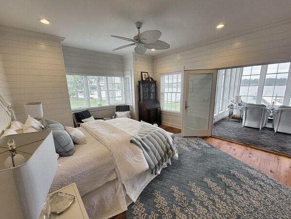 A bedroom with a large bed, a ceiling fan, a view of the outdoors through a sliding glass door, and a seating area with chairs. - Beautiful Sunset Views on Coldwater Lake!! (Coldwater)