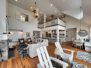 A spacious living area with a high ceiling, a staircase leading to an upper level, and a kitchen with bar seating. - Beautiful Sunset Views on Coldwater Lake!! (Coldwater)
