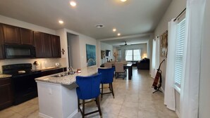 A modern kitchen with dark wooden cabinets, a granite countertop, and blue bar stools. - New Modern home only 11 miles from Downtown and the Pearl Brewery! (Converse)