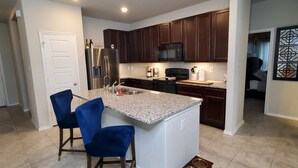 A modern kitchen with granite countertops, stainless steel appliances, and dark wood cabinets. There are two blue chairs and a small pet feeding station. - New Modern home only 11 miles from Downtown and the Pearl Brewery! (Converse)