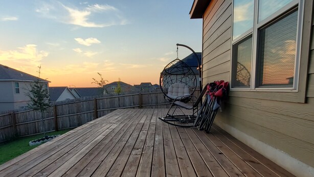 A wooden deck with a hanging chair and a stroller, a wooden fence, and houses in the background. - New Modern home only 11 miles from Downtown and the Pearl Brewery! (Converse)